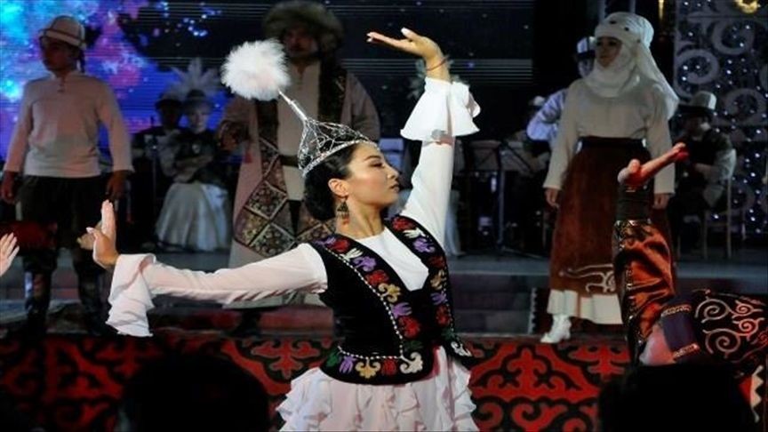 Dancer in traditional clothing performing on stage, with background performers in cultural attire.