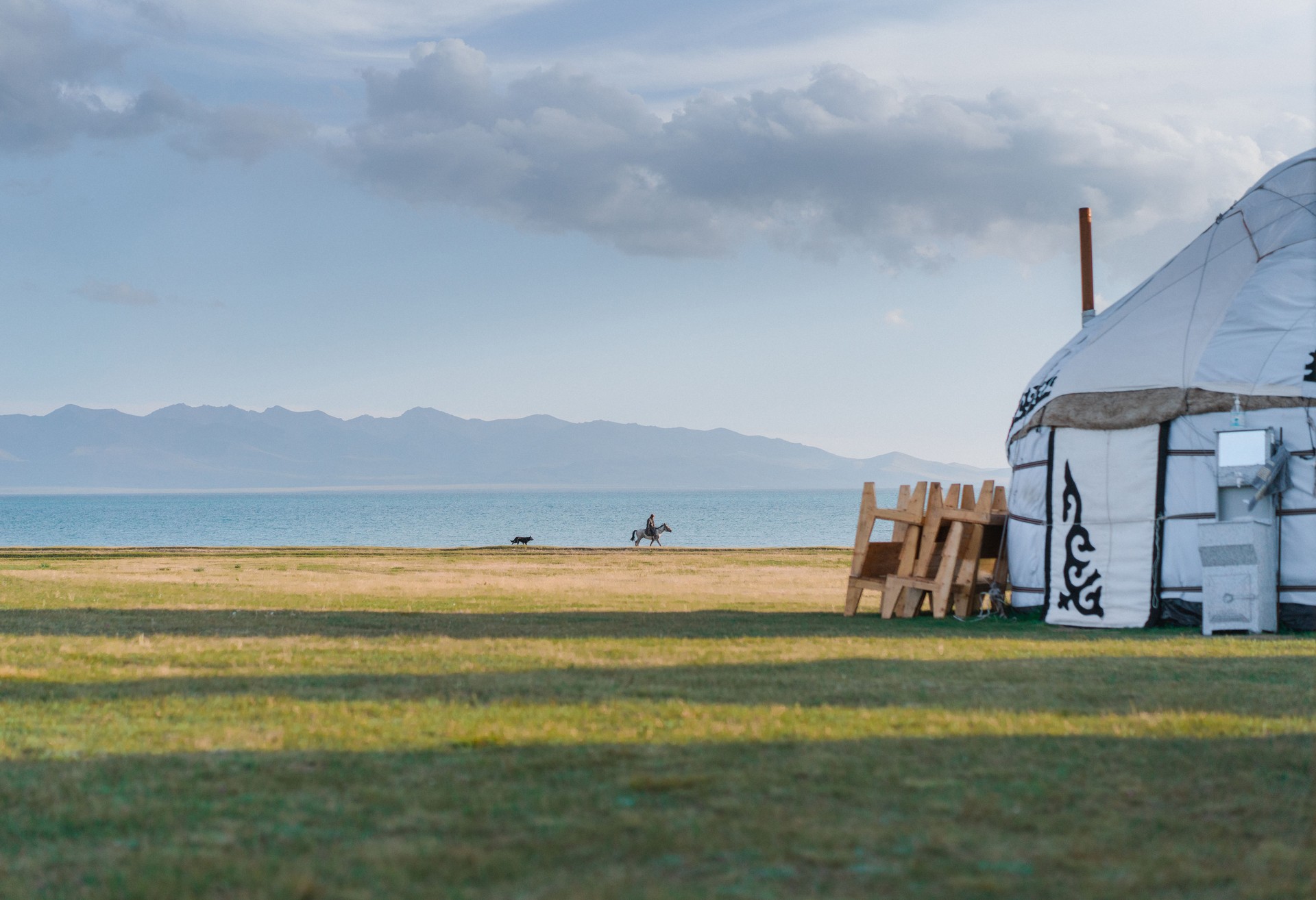 Scenic view of man on horse with dog running behind near yurts, Son-Kul lake in Kyrgyzstan